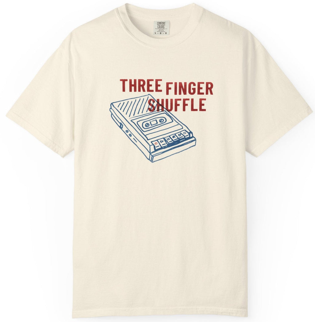 Beige t-shirt with a cassette tape graphic and 'Three Finger Shuffle' text on a white background