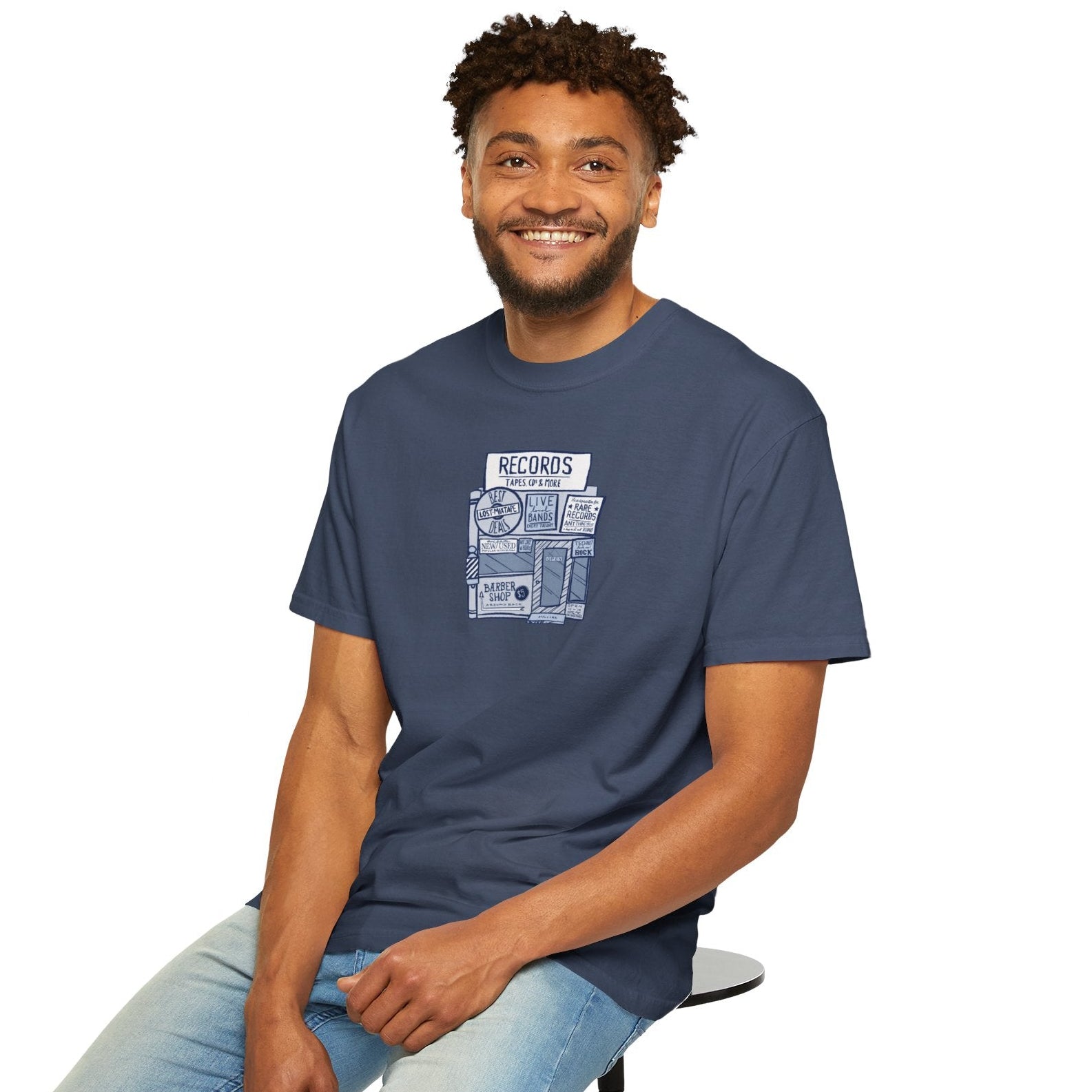Man sitting on a stool wearing a slate blue t-shirt with graphic design on a white background