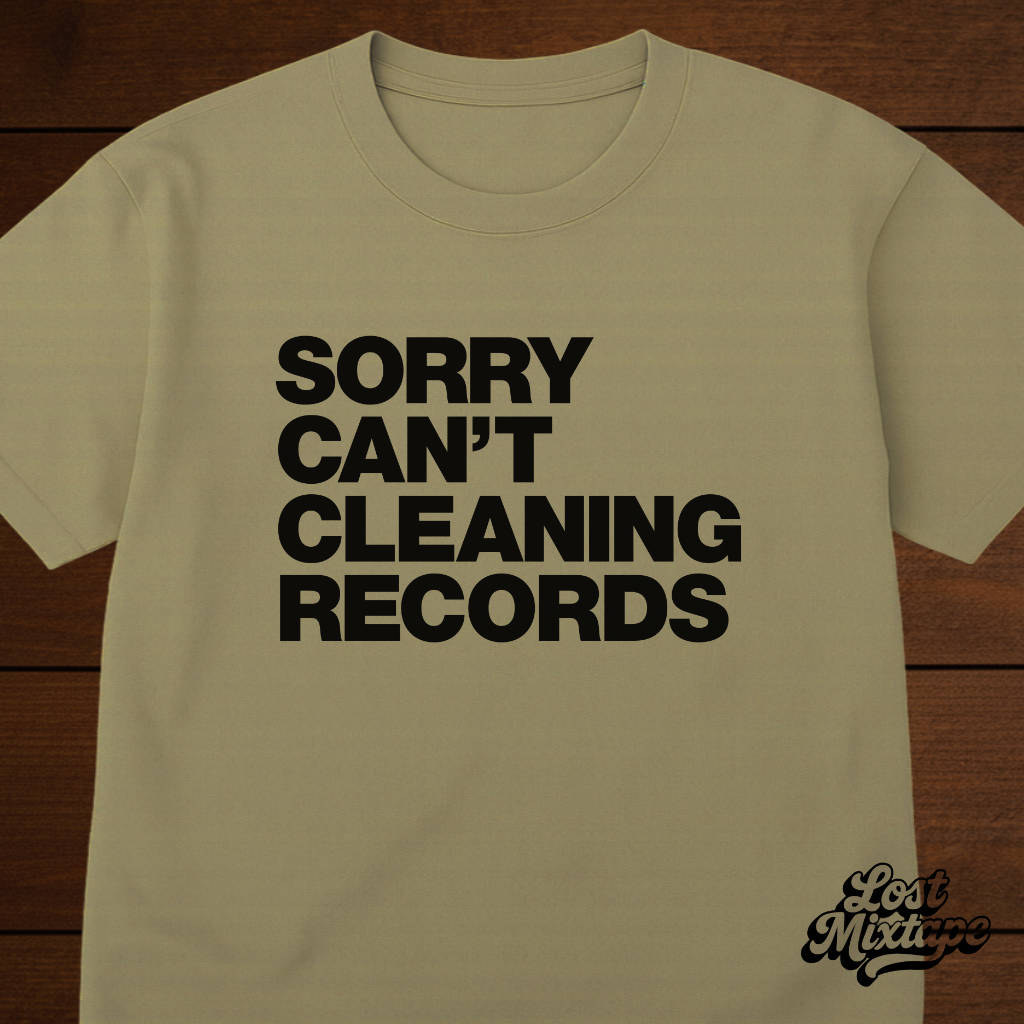 Beige t-shirt with black text 'SORRY CAN'T CLEANING RECORDS' on a wooden background
