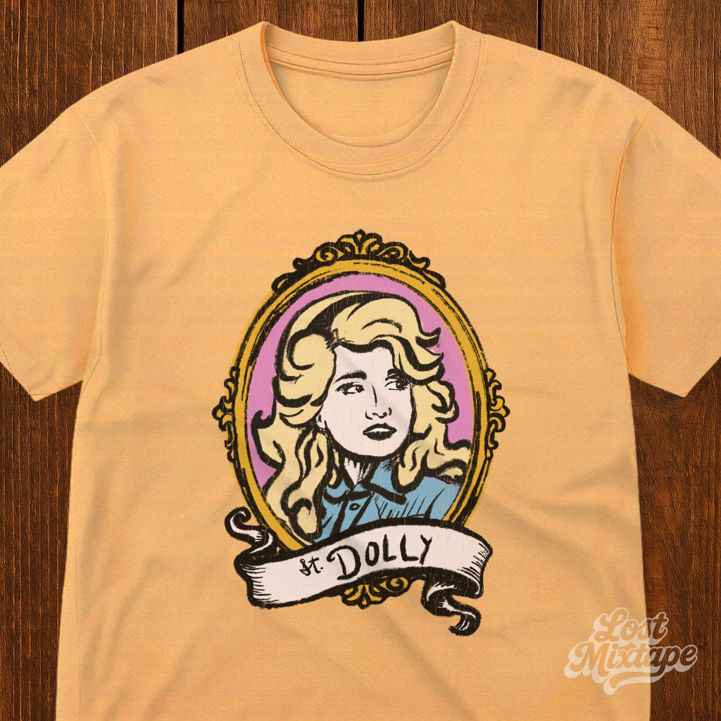Yellow t-shirt with a graphic of a woman's portrait and 'St. Dolly' text on a wooden surface.