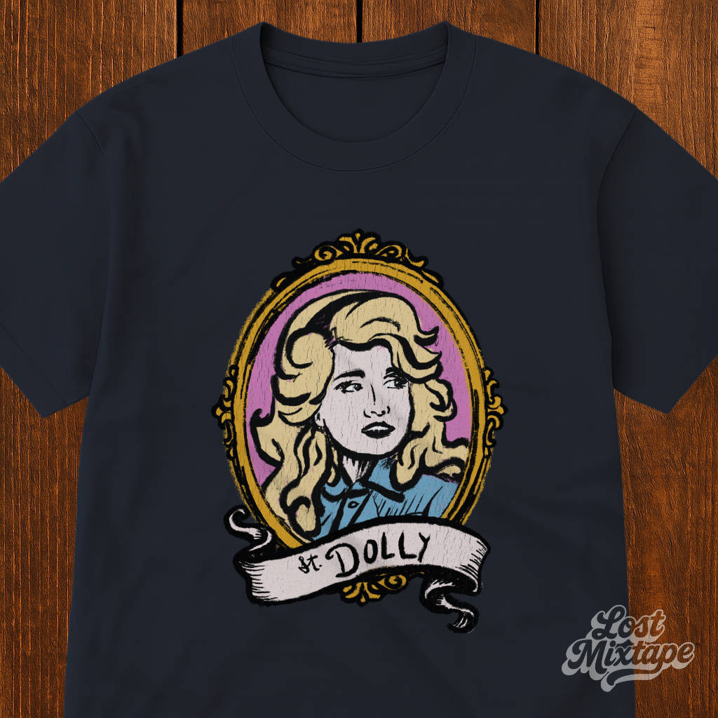 Black t-shirt with a graphic of a woman's portrait and 'St. Dolly' text on a wooden surface.