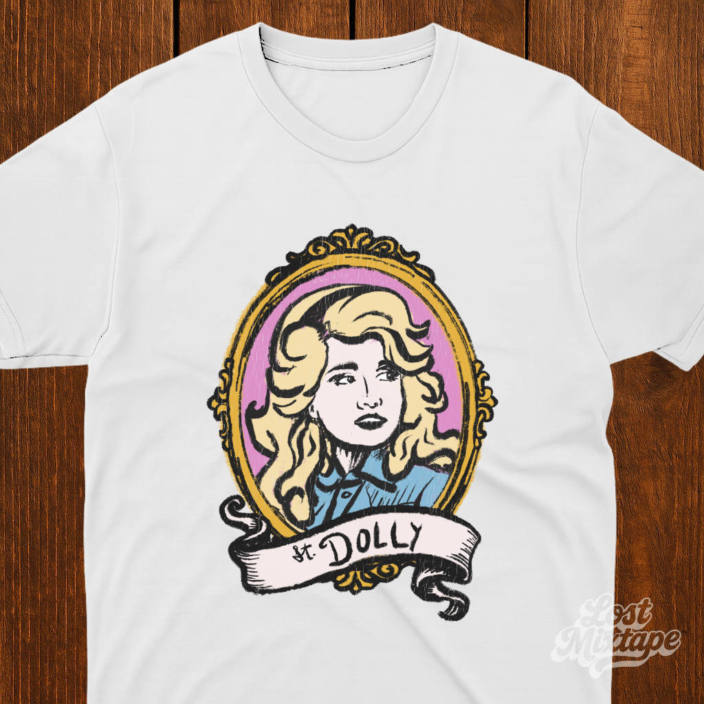 White t-shirt with a graphic of a woman's portrait and 'St. Dolly' text on a wooden surface.