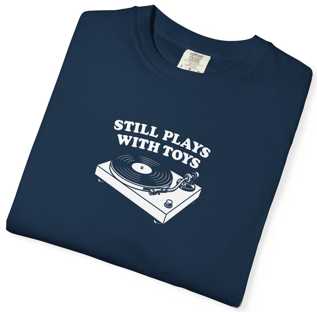 Folded navy blue t-shirt with a graphic of a turntable and text 'STILL PLAYS WITH TOYS' on a white background.